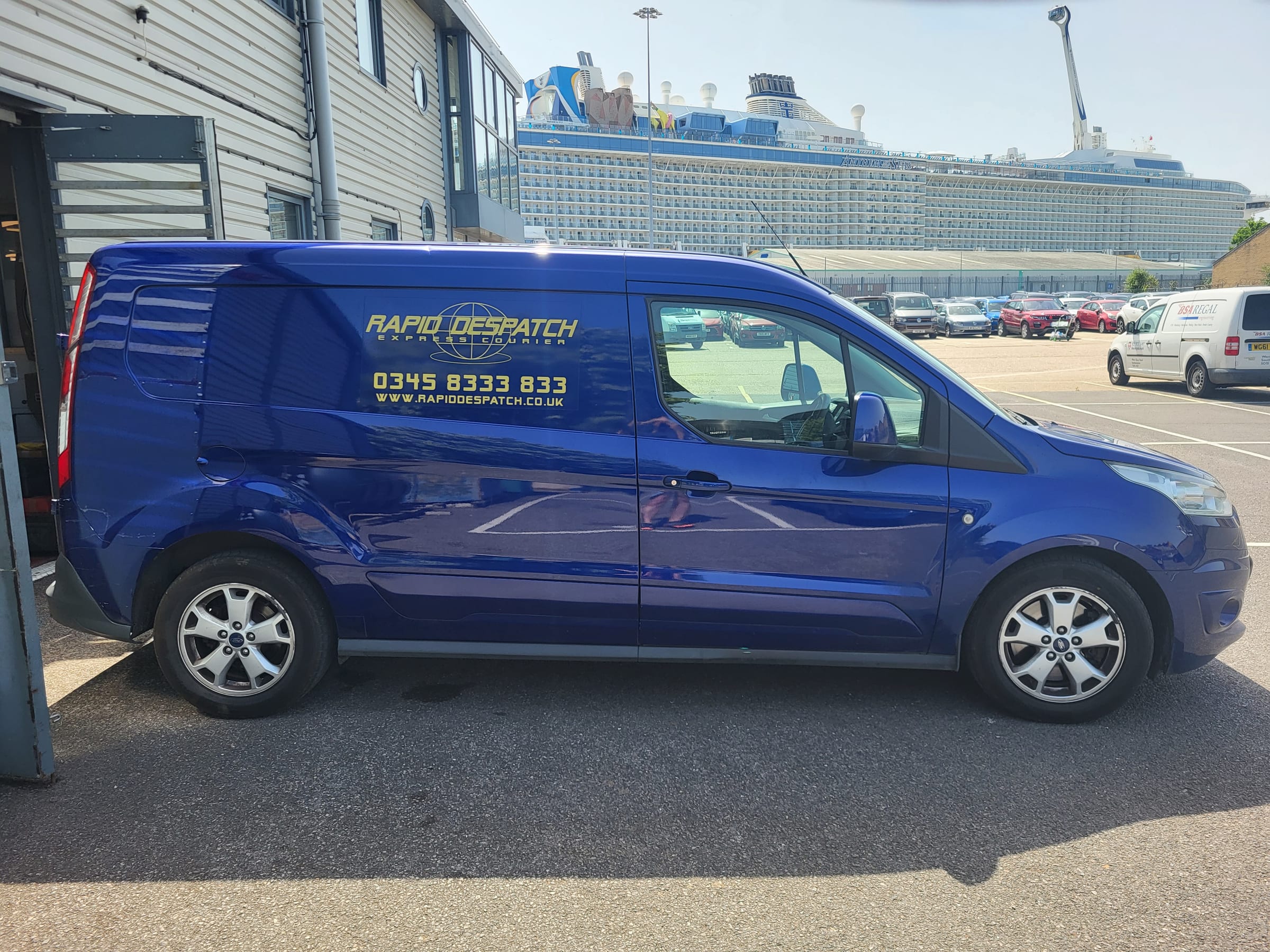 A blue Rapid Despatch van parked by a quayside, with a cruise ship behind