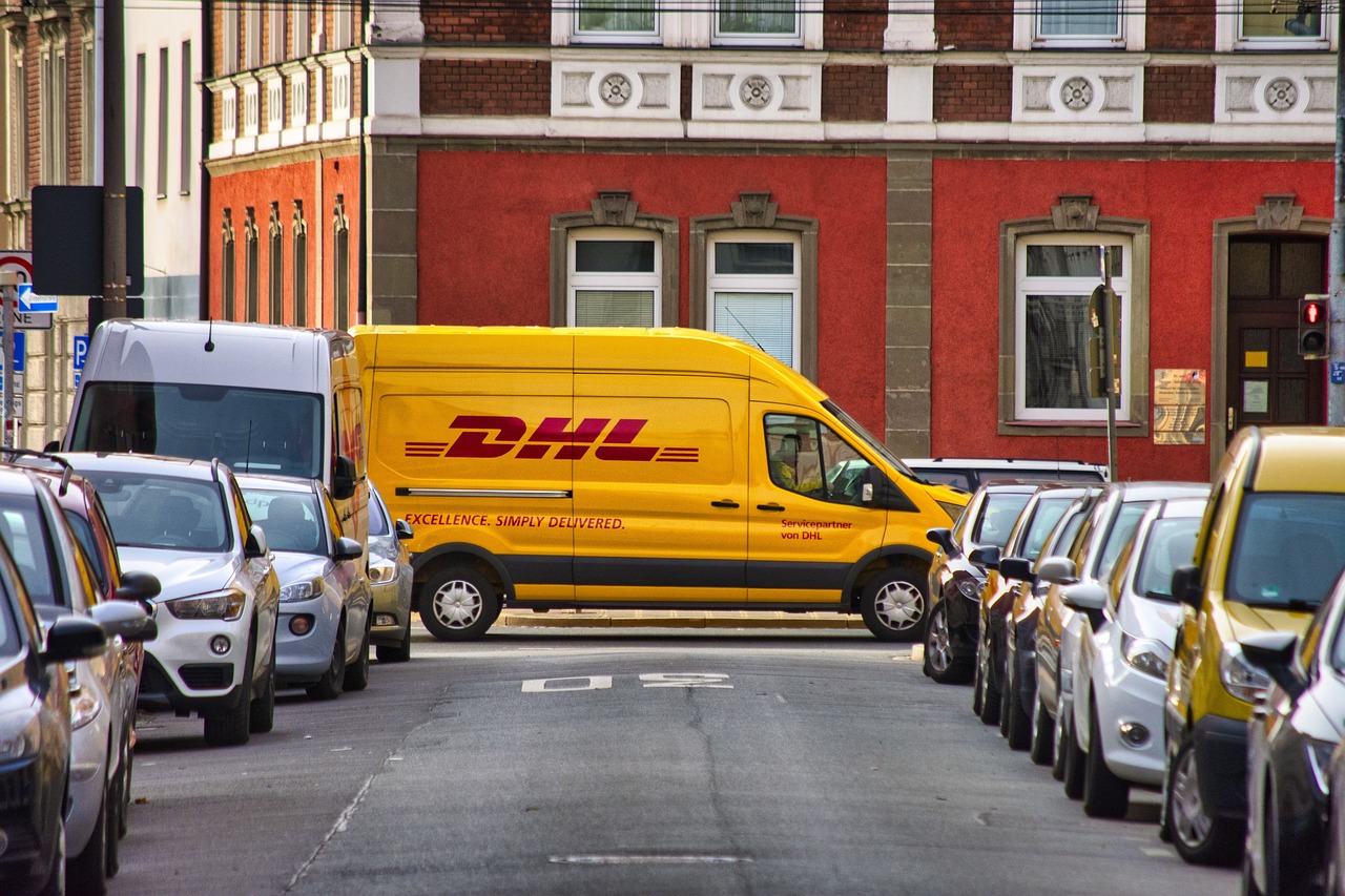 A yellow DHL van parked on a city street lined with cars