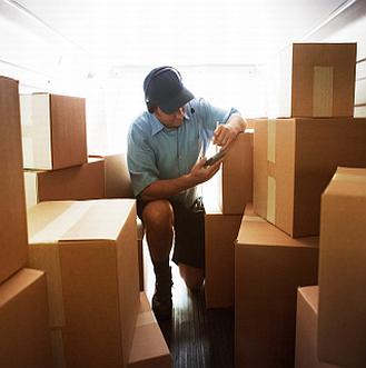 A delivery driver checking a parcel among stacked boxes in the back of a van