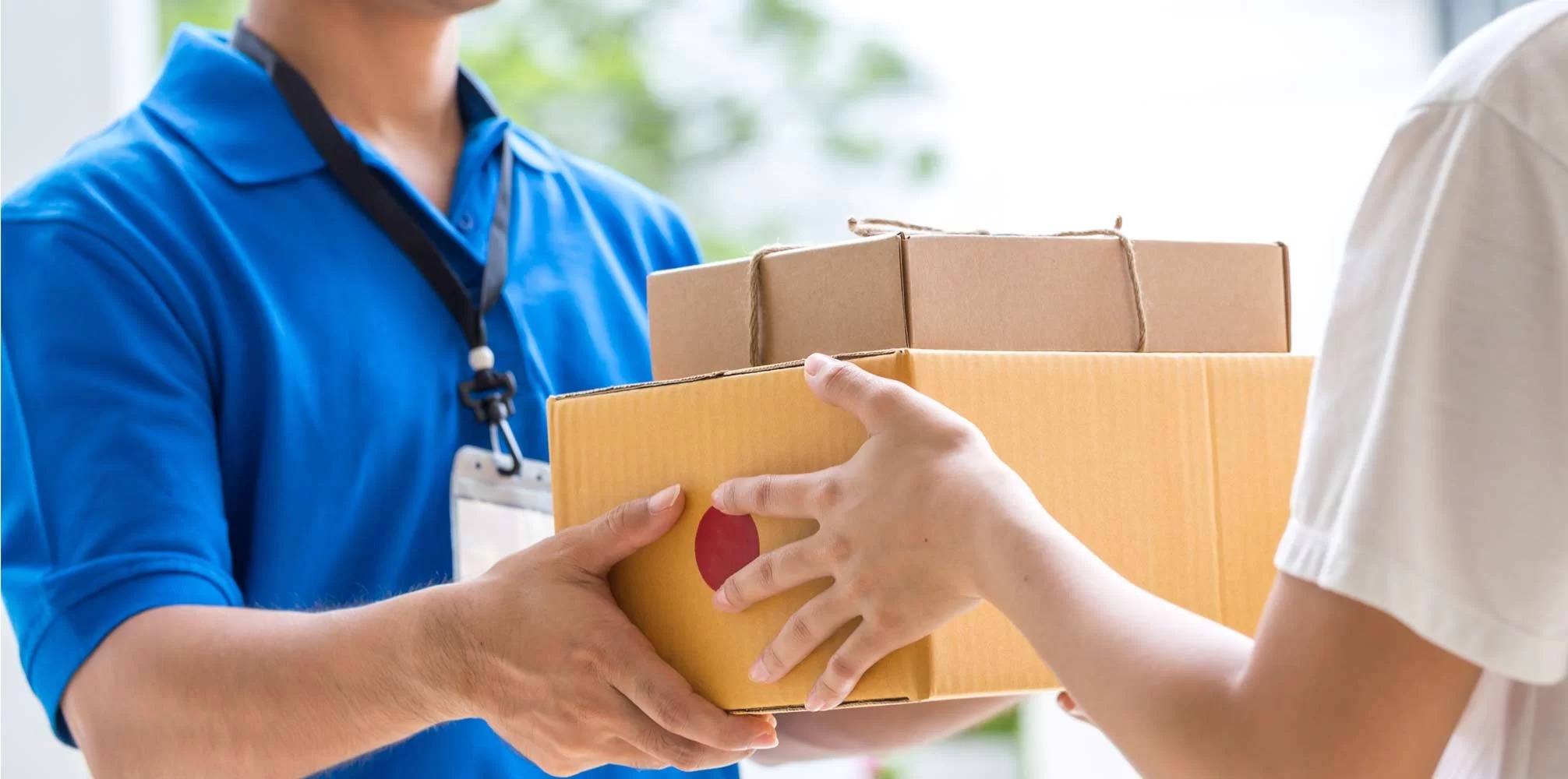 A courier in a blue polo shirt handing a cardboard box to a customer