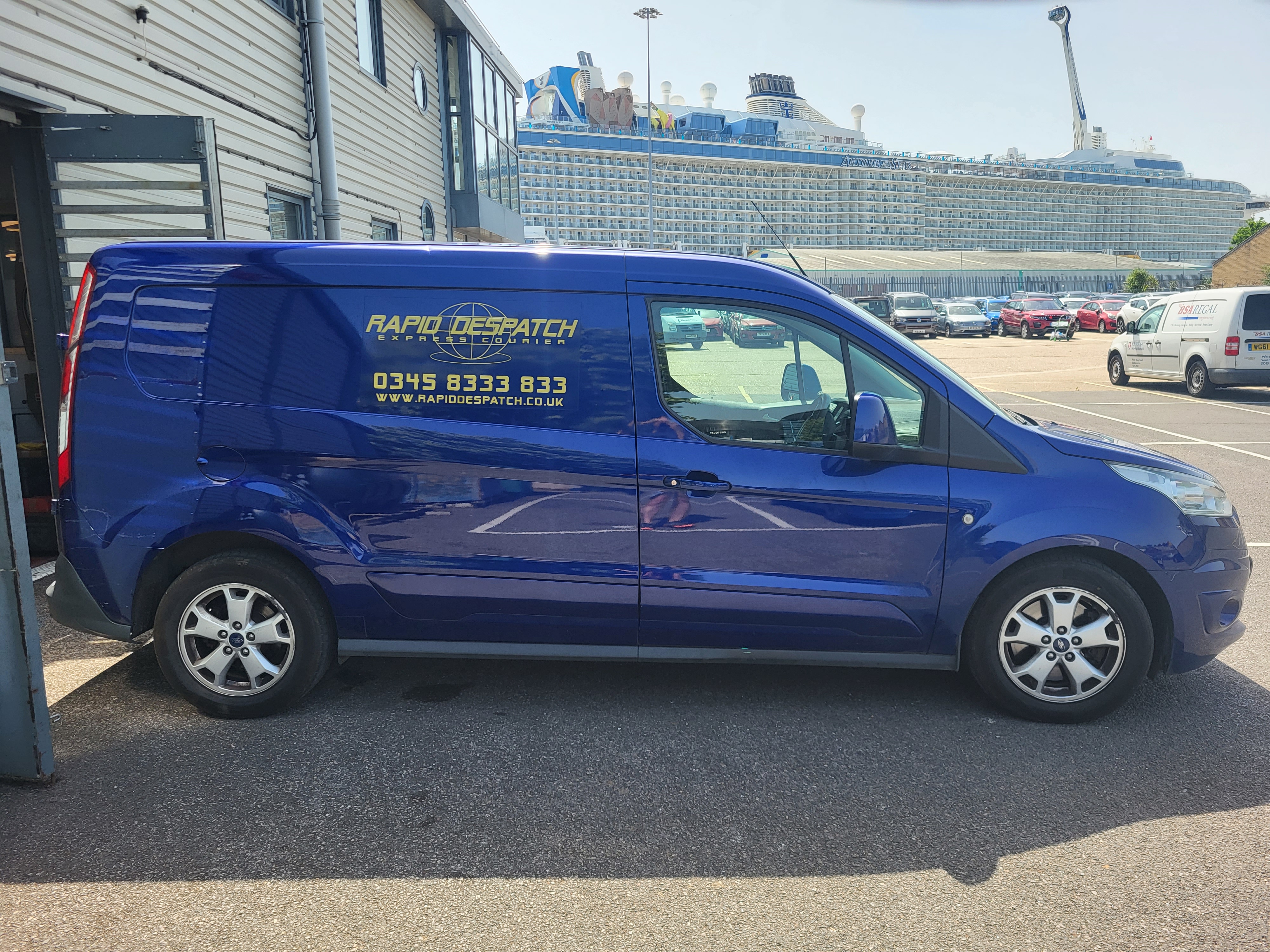 A blue Rapid Despatch van parked by a quayside, with a cruise ship behind