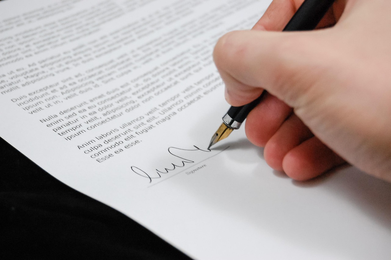 A hand signing a printed document with a fountain pen