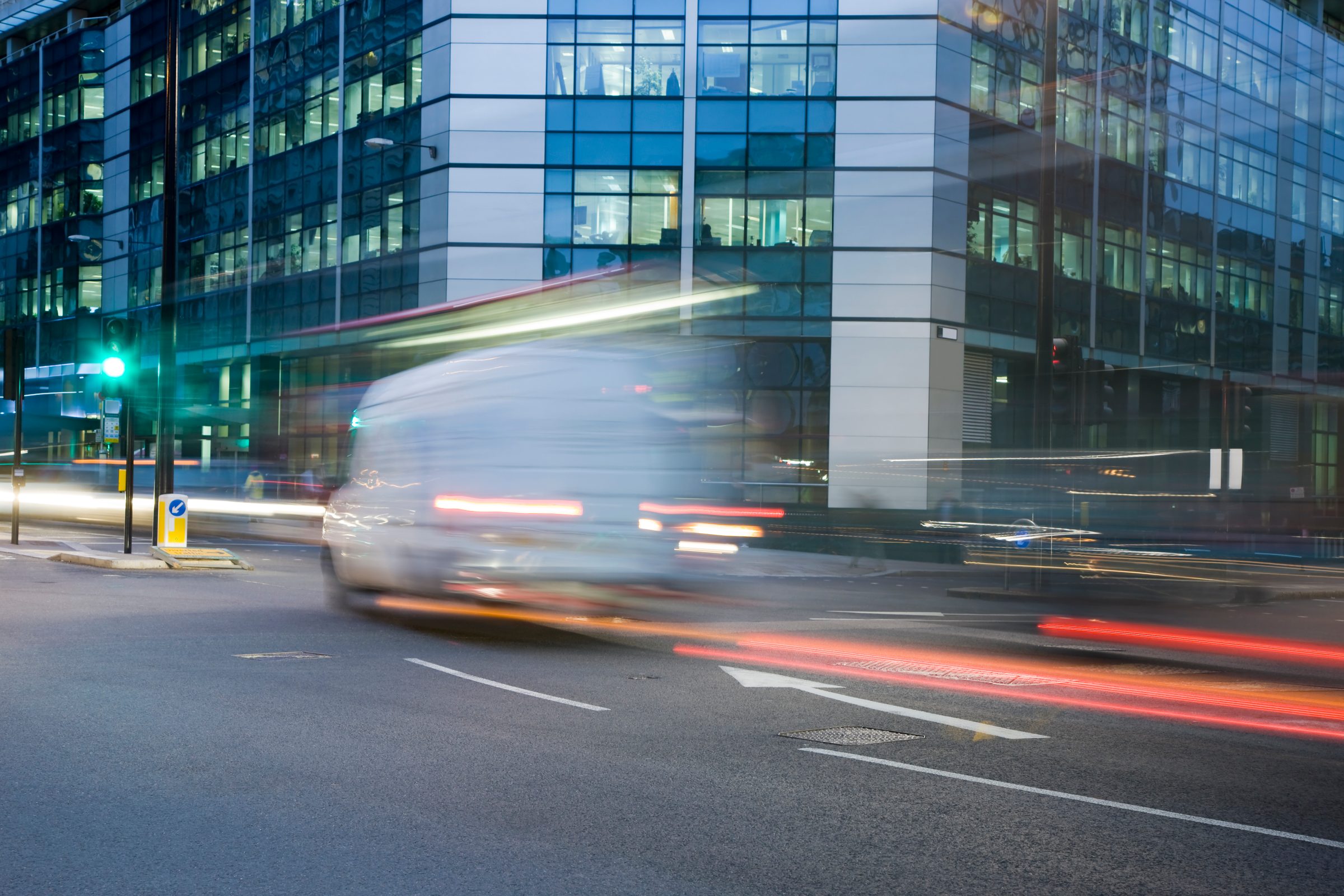 A van moving at speed past glass office buildings at dusk