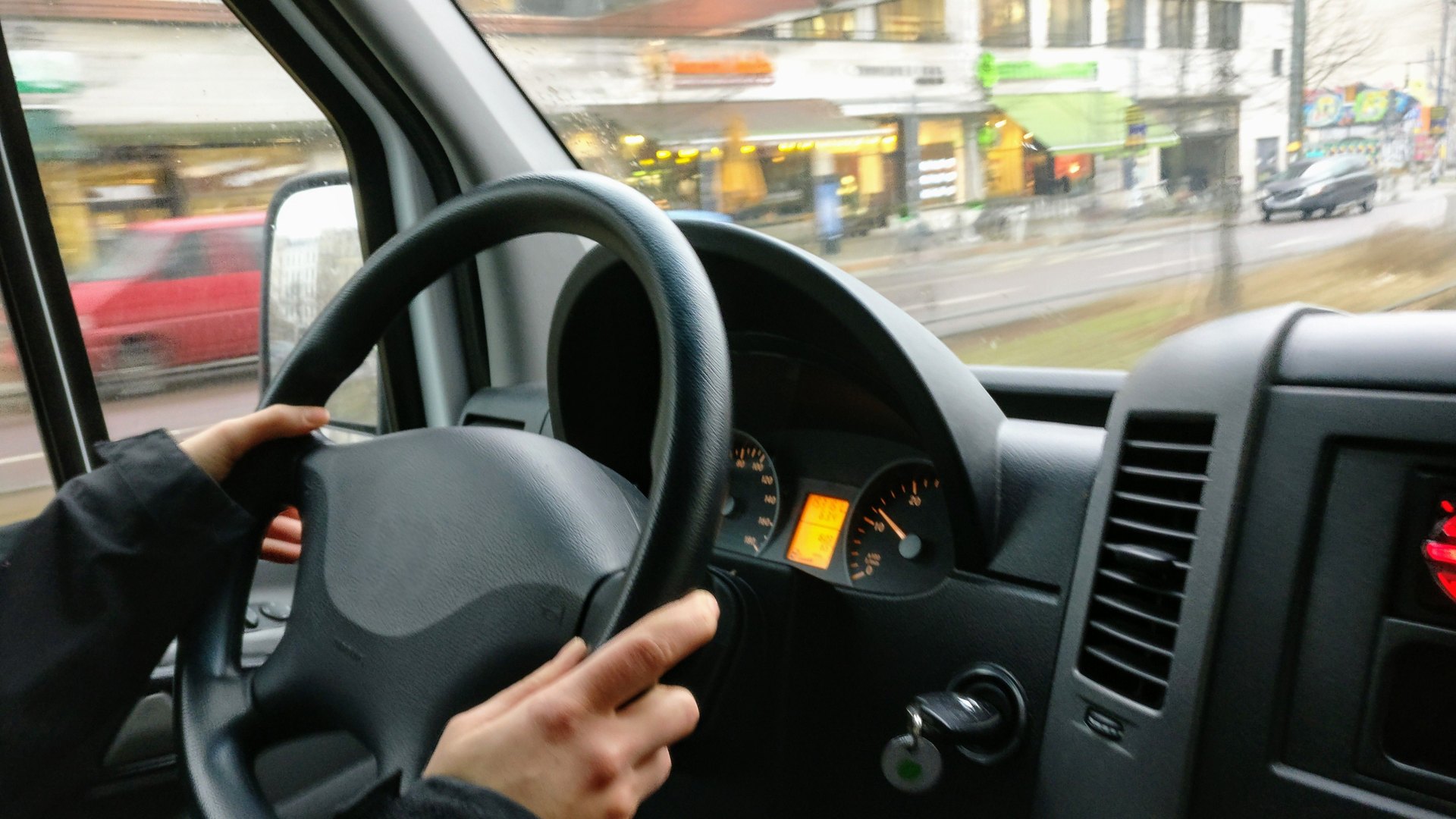 A driver's hands on the wheel of a van in city traffic