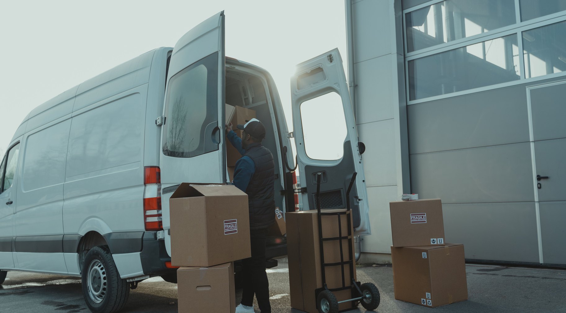 A courier loading boxes into a large van outside a warehouse