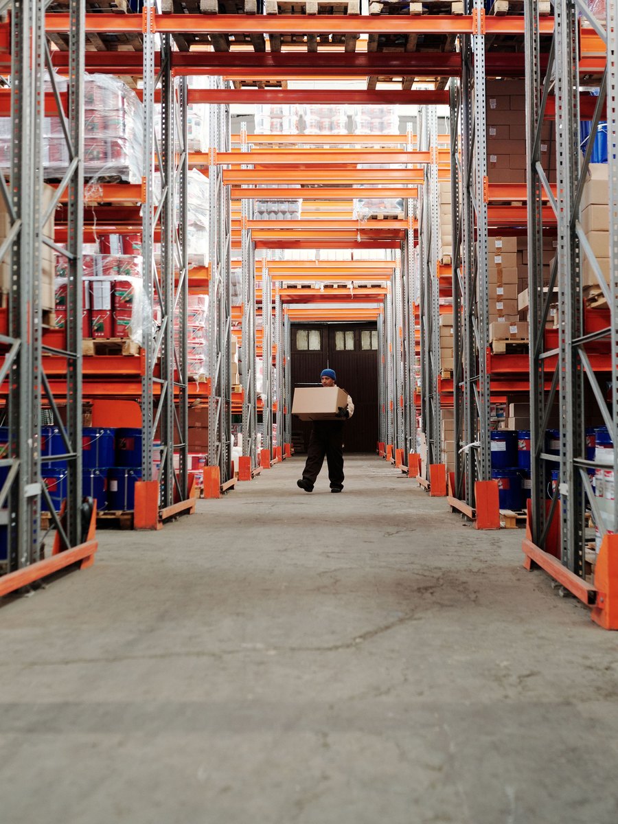 A worker carrying a box down a warehouse aisle