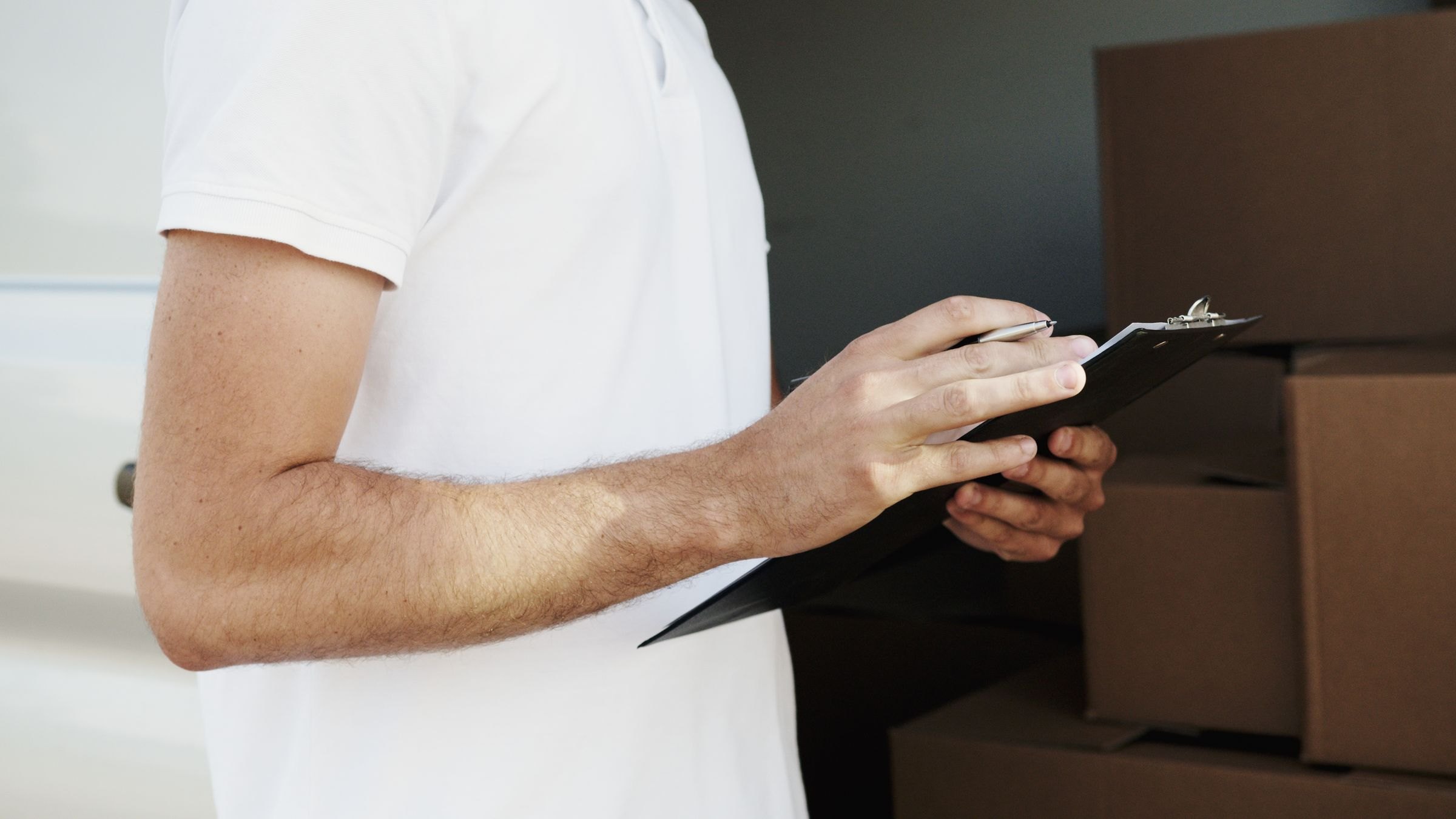 A courier checking a delivery list on a clipboard beside a loaded van