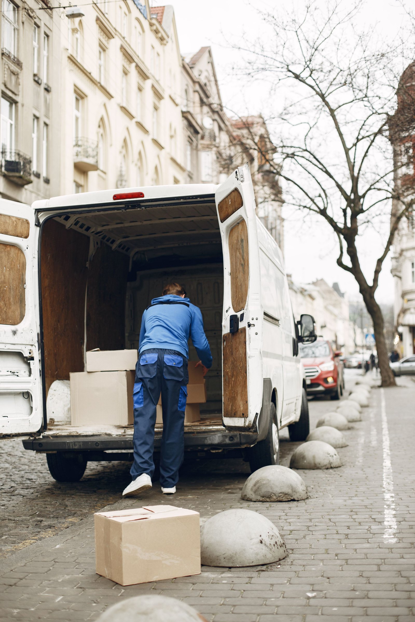 A courier loading boxes into the back of a van on a town street
